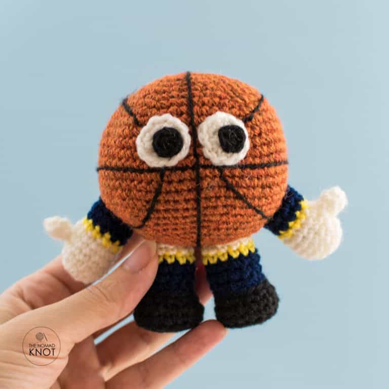 Photo of my hand holding the basketball mascot amigurumi in front of a blue background. Free crochet pattern.