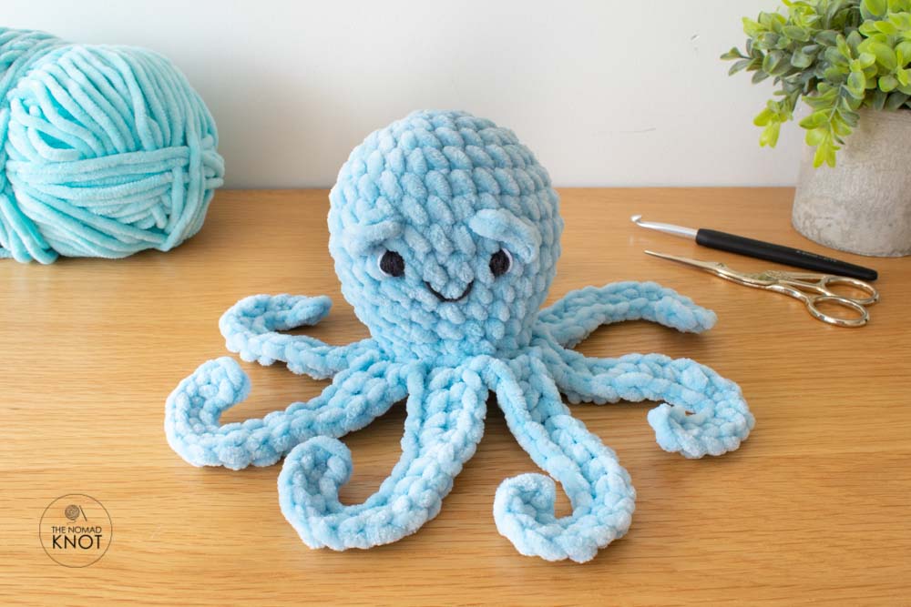 image feature crochet a blue octopus, on top of a shelf with a skein of yarn in one side and a small plant pot in the other