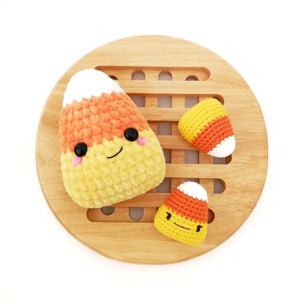 Large plush yarn candy corn with two smaller crochet candy corns on a hollow bamboo piece placed on a white surface.
