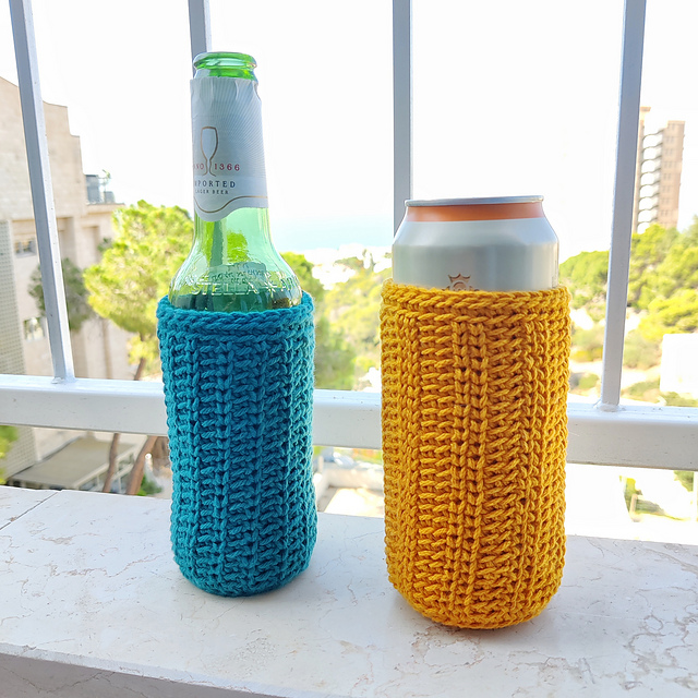 Two handmade crochet drink cozies are displayed side-by-side on a white balcony ledge. The cozy on the left is teal blue with a textured stitch and holds a green glass beer bottle. The cozy on the right is mustard yellow with a ribbed stitch and holds a silver aluminum can.