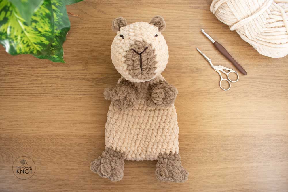 Easy Crochet Capybara Snuggler Free Pattern on top of a wooden table with yarn suplies on the side
