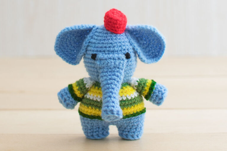a crochet elephant free pattern wearing a green and yellow shirt with a red hat on its head